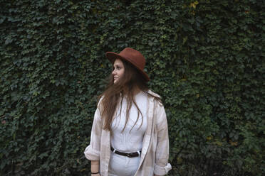 Young woman wearing hat standing in front of plants - VPIF09060