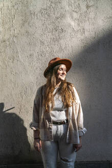Lächelnde Frau mit Hut und vor einer Wand stehend - VPIF09062