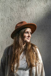Lächelnde junge Frau mit Hut und vor einer Wand stehend - VPIF09063