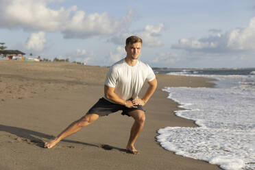 Young man stretching at beach - STF00002