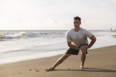Young man doing stretching exercise at beach - STF00003