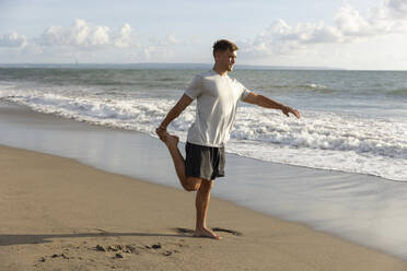 Man practicing stretching exercise at beach - STF00004