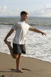 Young man stretching leg at beach - STF00005