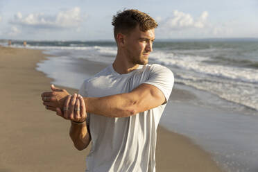 Young man stretching arm at beach - STF00007