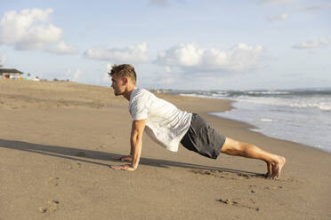 Young man exercising on sand at beach - STF00009