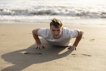 Man doing push-ups on sand at beach - STF00010