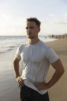 Young man standing with hands on hips at beach - STF00014