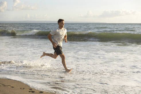 Smiling young man running in water at beach - STF00019