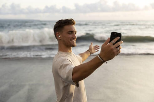 Happy man showing sea on video call through smart phone at beach - STF00025