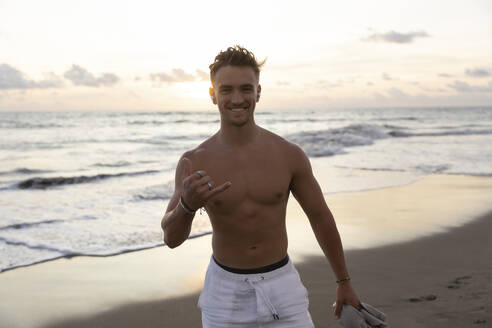 Happy young man gesturing Shaka sign at beach - STF00031