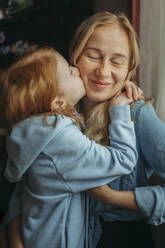 Girl kissing smiling mother at home - ANAF02553