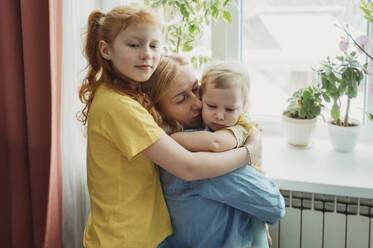 Mother and daughters hugging each other at home - ANAF02558