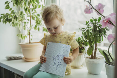 Girl sitting on window sill and showing drawing - ANAF02560