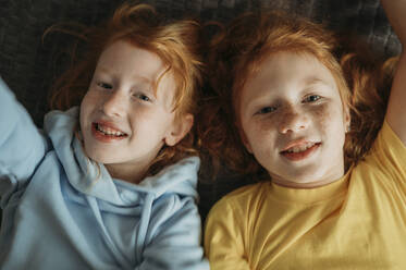 Smiling sisters lying on bed at home - ANAF02562