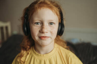 Smiling girl listening to music through wireless headphone at home - ANAF02563