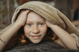 Smiling girl under blanket on bed - ANAF02571