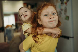Redhead girl giving piggyback ride to sister at home - ANAF02573