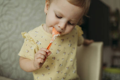 Girl eating porridge with spoon at home - ANAF02588