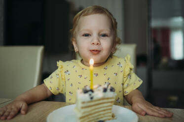 Smiling girl blowing candle on birthday cake at home - ANAF02591