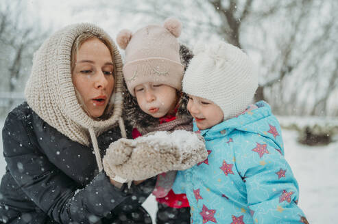 Mother and daughters blowing snow in winter park - ANAF02593