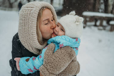 Happy mother kissing daughter in winter - ANAF02594