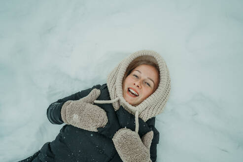 Smiling woman lying on snow in winter - ANAF02595