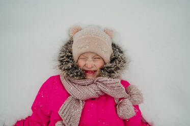 Smiling girl lying on snow in winter - ANAF02598