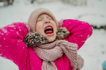 Playful girl with eyes closed catching snow with mouth in winter - ANAF02600