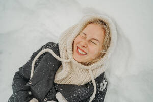 Smiling woman lying with eyes closed on snow - ANAF02604