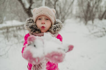 Girl blowing on snow in winter park - ANAF02605