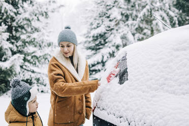 Woman standing near son and scraping snow from car - VSNF01493