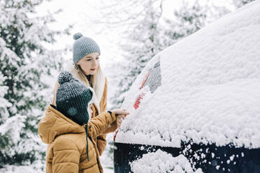 Boy helping mother to clear snow from car - VSNF01495