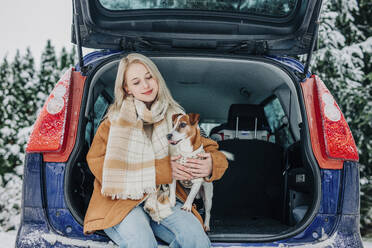 Smiling woman sitting in car trunk with pet dog - VSNF01496