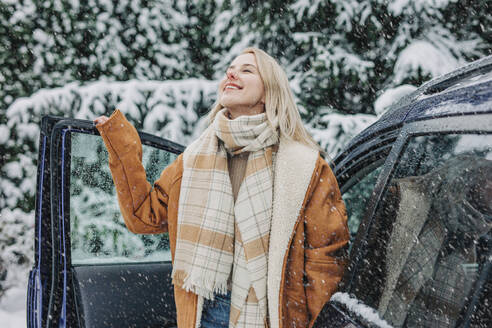 Smiling woman standing by car door on snowy day - VSNF01501