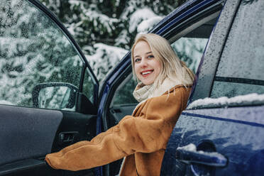 Happy woman with blond hair getting out of car - VSNF01502