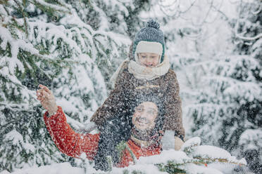 Happy man carrying son on shoulders near tree on snowy day - VSNF01504