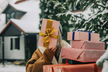 Woman holding Christmas gift over face near tree - VSNF01516