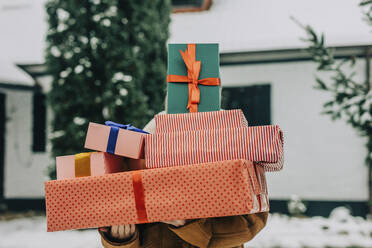 Woman covering face with Christmas presents in winter - VSNF01518