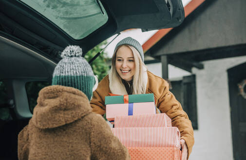 Lächelnde Mutter zeigt ihrem Sohn Weihnachtsgeschenke in der Nähe des Autos - VSNF01526