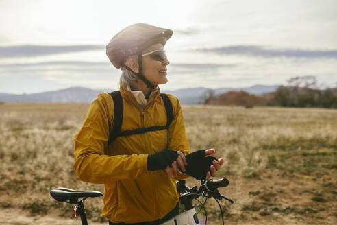 Smiling woman standing near mountain bike at field - EBSF04298