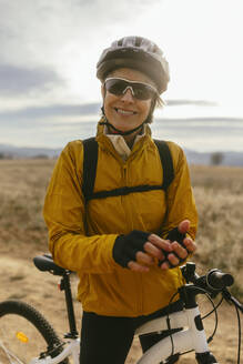 Smiling woman standing with mountain bike at field - EBSF04299