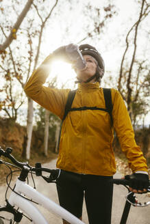 Woman drinking water from bottle near mountain bike in forest - EBSF04301