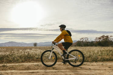 Woman riding mountain bike near field under sky - EBSF04304