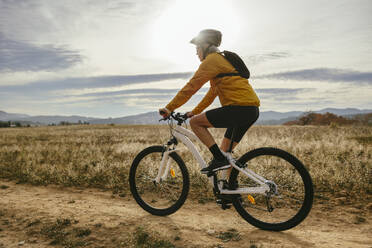 Woman riding mountain bike near field at sunset - EBSF04305