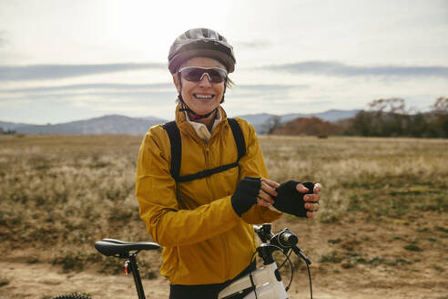 Smiling woman wearing helmet and standing with mountain bike near field - EBSF04307