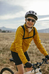 Happy woman riding mountain bike in front of field - EBSF04309