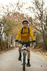 Woman riding mountain bike on road in forest - EBSF04310