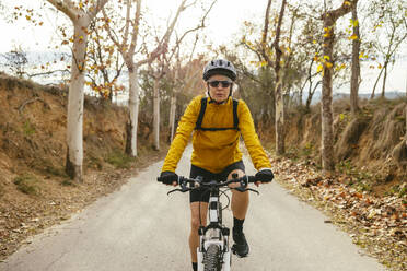 Woman riding mountain bike on road near trees in forest - EBSF04311