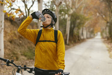 Woman standing with mountain bike and drinking water in forest - EBSF04313