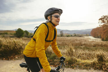 Mature woman riding mountain bike near field - EBSF04319